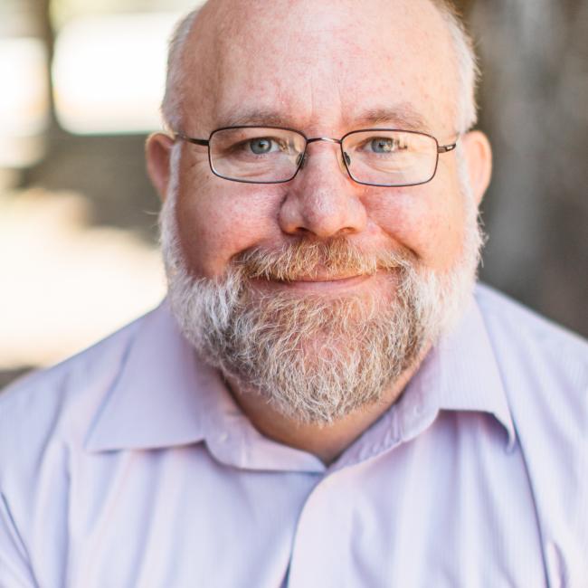 Gary Miller in a light blue button-up shirt, set against a softly focused natural outdoor background.