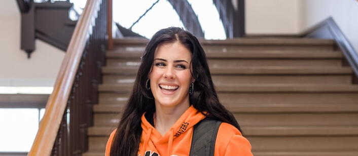 Girl in Oregon State University sweatshirt smiles and holds backpack