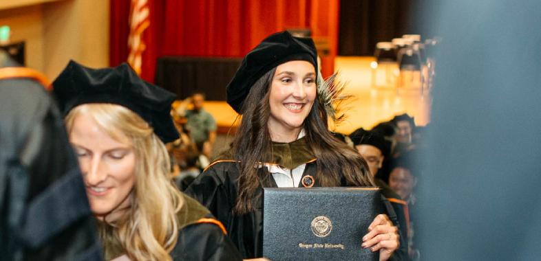 A young woman smiles with her diploma at graduation