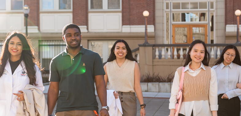 students walk towards camera in the sunlight behind college of pharmacy building