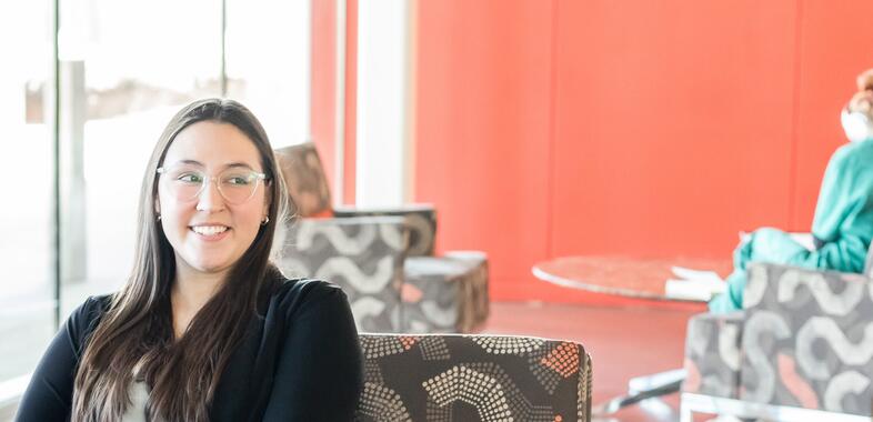 A woman sits in a chair with her arms folded in an upscale office building