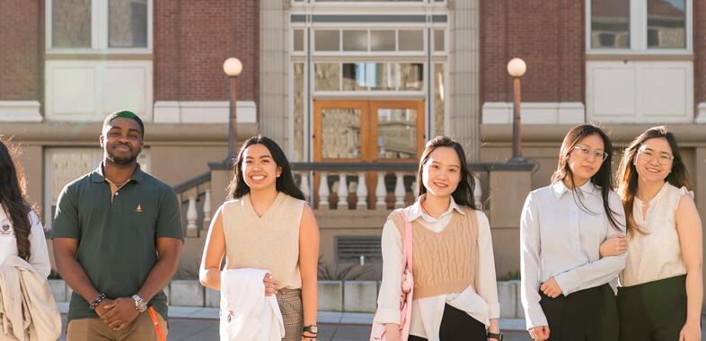 A group of students stand outside at sunset by the college of pharmacy, smiling at the camera.