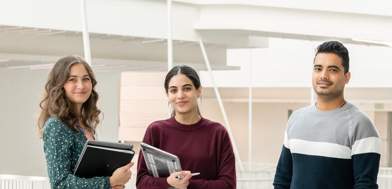 Three students smile at the camera while standing on a catwalk in the RLS Building