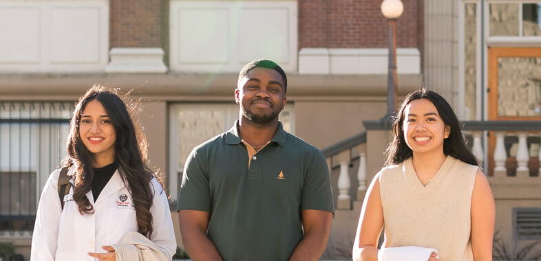 Three students smile and look at camera, smiling outside.