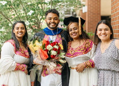 A family smiles proudly next to their graduate