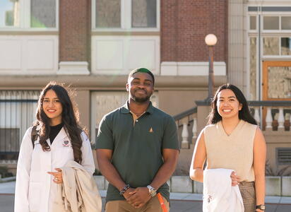 Three students smile and look at camera, smiling outside.